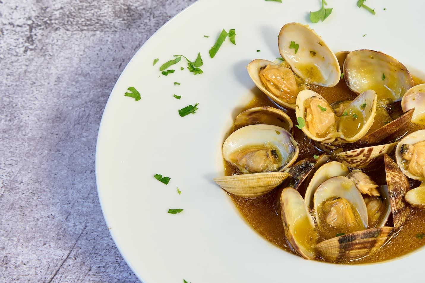 Almejas a la marinera en plato blanco decorado con perejil